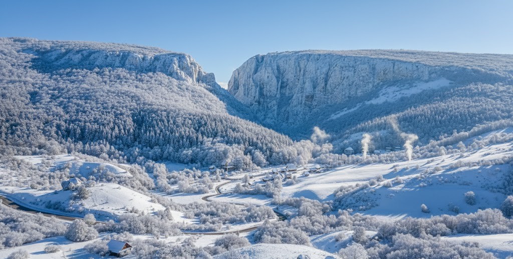 Panoramic winter view of Cheile Turzii (Turda Gorge) in Romania, featuring massive snow-covered limestone cliffs, a frosted forest, and a winding road in the valley.
