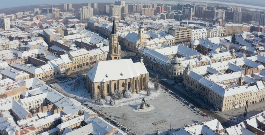 Ultra-wide aerial view of Cluj-Napoca city center in winter, featuring the snow-covered St. Michael's Church and Unirii Square under a clear sky.