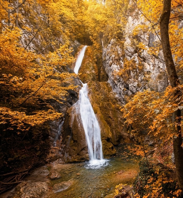 A beautiful two-stepped waterfall in the Locva Mountains of Romania during autumn, featuring golden leaves, mossy rocks, and a clear forest stream.